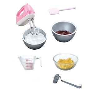 Op de afbeelding: Een set miniatuur keukengerei en ingrediënten voor het bakken, waaronder een roze handmixer, een maatbeker, een spatel, een kom met chocolade, een kom met beslag en een aardappelstamper.