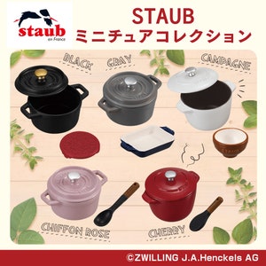 May include: A collection of Staub mini cocotte enamel cast iron cookware in various colors, including black, gray, white, pink, and red. The cocotte lids are off, revealing the interior of the pots. The text "STAUB ミニチュアコレクション" is visible in the image.