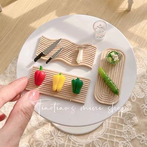Puede incluir: Un juego de cocina en miniatura con tablas de cortar de madera, cuchillos y verduras. El juego incluye un pimiento rojo, amarillo y verde, un pepino y un champiñón. El juego es perfecto para casas de muñecas o juegos en miniatura.