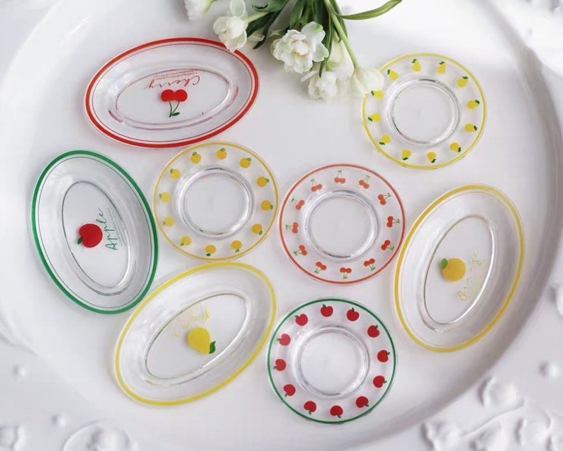 Op de afbeelding: Set van acht kleine glazen borden met kleurrijke randen en fruitontwerpen. De borden hebben een kersen-, appel-, citroen- en aardbeienthema.