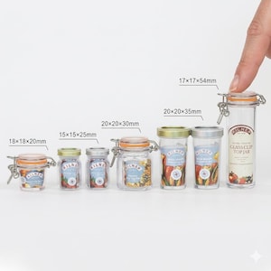 Può includere: Una collezione di barattoli di vetro trasparente Kilner con chiusure e coperchi in metallo. I barattoli variano in dimensioni, da 18x18x20mm a 17x17x54mm. Ogni barattolo contiene cibo e ha un'etichetta.