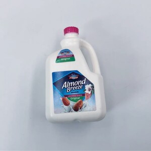 May include: A white plastic jug of Almond Breeze unsweetened almond milk with a pink cap and a handle. The label features a blue diamond with the brand name and images of almonds.