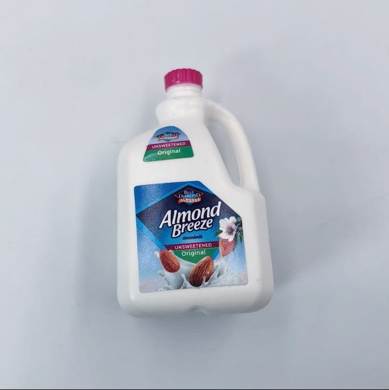 May include: A white plastic jug of Almond Breeze unsweetened almond milk with a pink cap and a handle. The label features a blue diamond with the brand name and images of almonds.