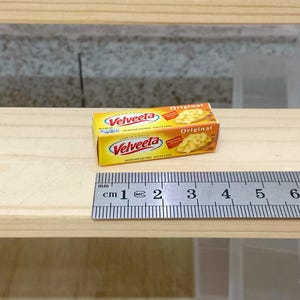Könnte beinhalten: Zwei Schachteln Velveeta-Käseprodukt, eine auf der anderen. Die Schachteln sind gelb mit rotem und weißem Text. Die obere Schachtel trägt die Aufschrift "Original" und die untere Schachtel die Aufschrift "Velveeta Original". Unter den Schachteln befindet sich ein Lineal, das zeigt, dass die Schachteln etwa 5 cm lang sind.
