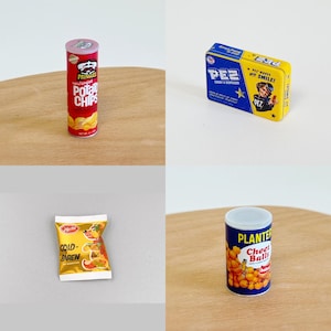 May include: A collection of miniature snack food cans and boxes. The cans are red and white with the brand names "Pringles", "Planters", and "Cheetos". The boxes are blue and yellow with the brand names "PEZ" and "Cold-Baren".