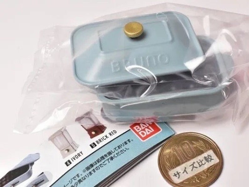 May include: A miniature light blue rectangular casserole dish with a lid and a gold-colored knob, sealed in a clear plastic bag. The item is accompanied by a Bandai product information card and a Japanese 10 yen coin for scale comparison.