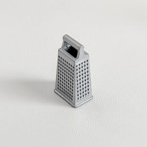 Peut inclure: Une petite râpe de couleur argentée, de forme rectangulaire, avec une poignée sur le dessus. La râpe comporte de nombreux petits trous et une surface texturée pour râper les aliments. Un ustensile de cuisine pratique.