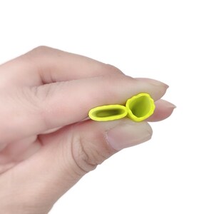 May include: Two yellow silicone pastry tips are held in a hand against a white background. One tip is a long oval shape, and the other is a flower shape. The tips are for decorating cakes and pastries.