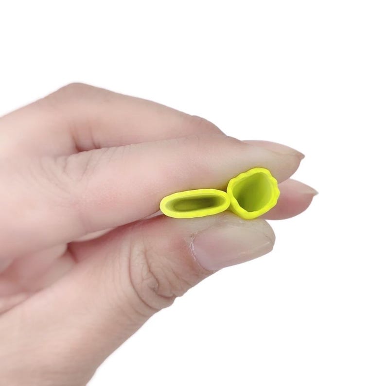 May include: Two yellow silicone pastry tips are held in a hand against a white background. One tip is a long oval shape, and the other is a flower shape. The tips are for decorating cakes and pastries.
