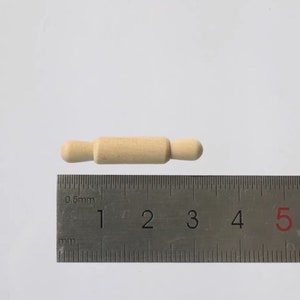 Puede incluir: Un rodillo de madera que mide aproximadamente 7,5 cm de largo. El rodillo es de color marrón claro y tiene extremos redondeados.