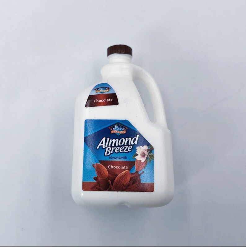 May include: A white plastic jug of Almond Breeze chocolate almond milk. The jug has a brown cap and a handle. The label features a blue diamond with the words "Almond Breeze" and "Chocolate" with an image of almonds.