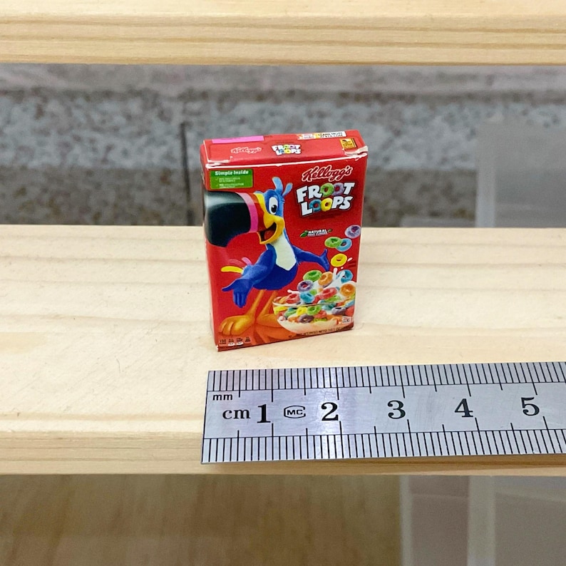 May include: Miniature Kellogg's Froot Loops cereal box. The red box features the Froot Loops logo and a cartoon toucan. The box is next to a ruler, with the box measuring approximately 1 inch in height.