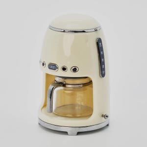 Peut inclure: Cafeti&egrave;re de style r&eacute;tro cr&egrave;me avec une carafe en verre. L'appareil dispose d'un affichage num&eacute;rique indiquant "08:00" et d'un indicateur de niveau d'eau. La cafeti&egrave;re a une garniture et une base chrom&eacute;es.