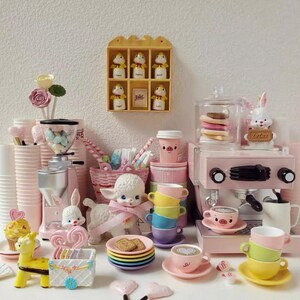 Pode incluir: Uma cole&ccedil;&atilde;o de miniaturas e acess&oacute;rios cor-de-rosa e pastel com tema de cozinha e caf&eacute;. Inclui uma m&aacute;quina de caf&eacute; expresso de brinquedo, x&iacute;caras, pires, um moedor de caf&eacute; e figuras decorativas de animais e sobremesas.