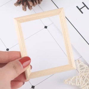 Op de afbeelding: Een klein, natuurlijk houten fotolijstje met een eenvoudig ontwerp. Het lijstje wordt in de hand gehouden en is klaar om te worden gebruikt voor een kleine foto of kunstwerk.
