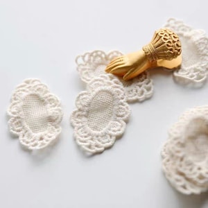 May include: Four white oval lace doilies with scalloped edges. A gold metal decorative paperweight in the shape of a hand is holding down two of the doilies.