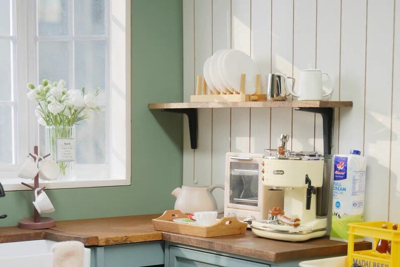 May include: A white and cream colored espresso machine with a chrome drip tray and a milk frother. The machine is sitting on a wooden countertop next to a toaster oven and a carton of milk. There is a wooden shelf above the countertop with white plates and a white mug.