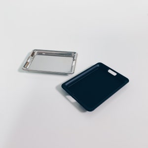 Pode incluir: Duas bandejas de servir, uma prateada e outra preta, sobre um fundo branco.