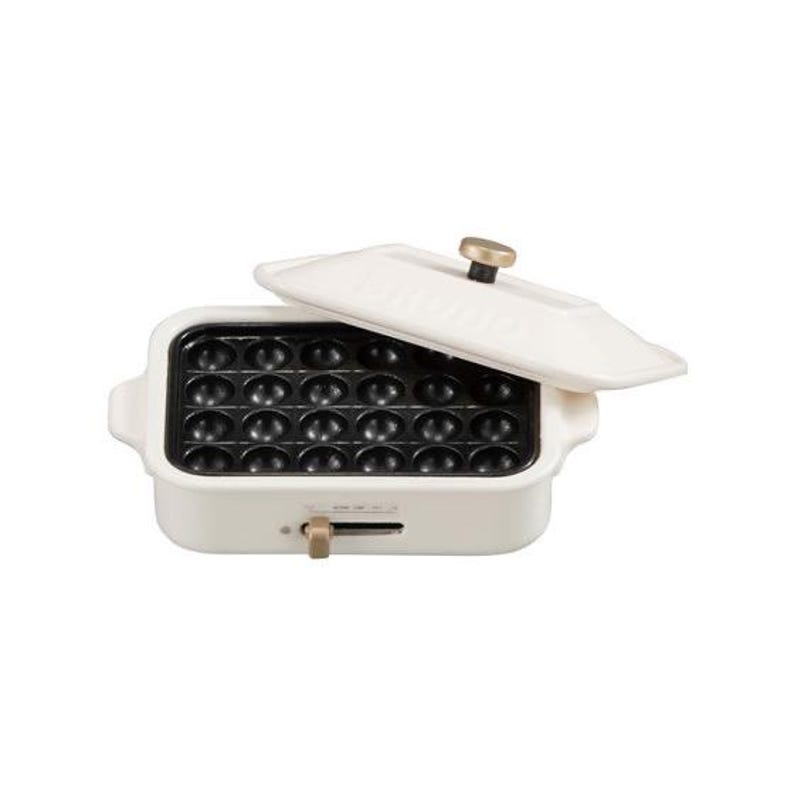May include: A cream-colored electric takoyaki maker with a black non-stick plate featuring twenty-four circular molds. The unit includes a matching cream lid with a gold-toned knob and a gold-toned sliding temperature control switch on the front.