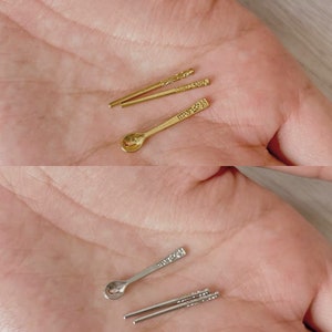 Könnte beinhalten: Zwei Sätze Miniatur-Essstäbchen und Löffel aus Gold und Silber. Die Essstäbchen sind mit einem Blumenmuster verziert. Die Löffel haben eine abgerundete Schale und einen dekorativen Griff.