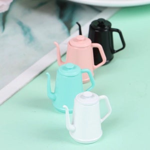 May include: Four miniature teapots in different colors: black, pink, light blue, and white. The teapots have a classic design with a spout and handle.