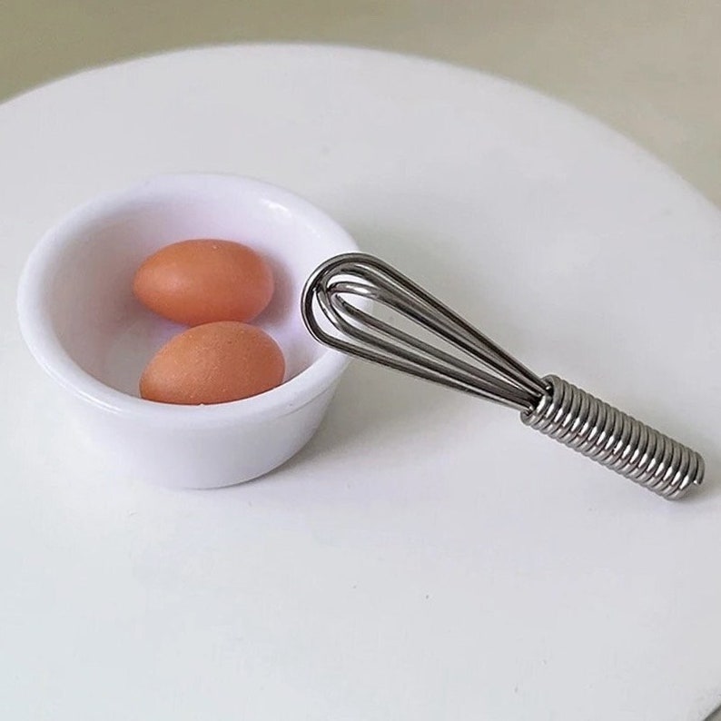 May include: Two brown eggs in a white bowl next to a silver whisk.