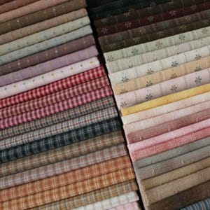 Op de afbeelding: Een verzameling van stoffenresten in verschillende kleuren en patronen, waaronder ruit, gingham en bloemenprints. De stoffen zijn gerangschikt in stapels, waarbij de verschillende patronen en kleuren een visueel aantrekkelijk geheel vormen.