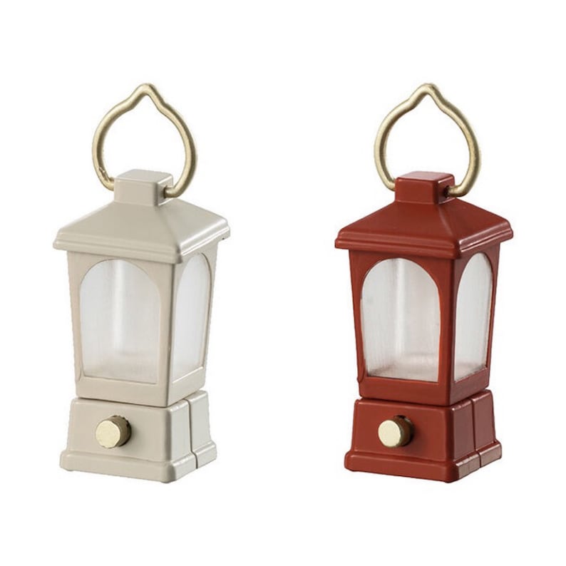 May include: Two miniature lanterns, one white and one red, with a gold handle and a clear glass window. The lanterns are on a white background.
