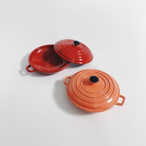 May include: Two red and orange ceramic cookware lids with black knobs. The lids are round and have a slightly raised rim.