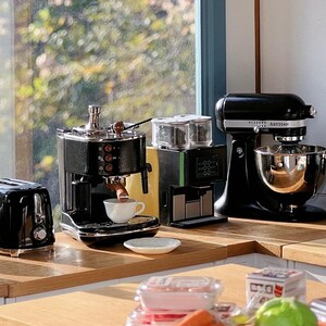 Peut inclure: Une collection d'appareils de cuisine noirs, dont un grille-pain, une machine &agrave; expresso, une cafeti&egrave;re, un batteur sur socle et une bouilloire, est dispos&eacute;e sur un comptoir en bois. Une tasse blanche est sous la machine &agrave; expresso.