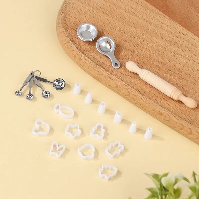 May include: Miniature baking set with a wooden rolling pin, metal measuring spoons, and various white plastic cookie cutters in different shapes. Includes small metal bowls and icing tips. Perfect for dollhouses or craft projects.