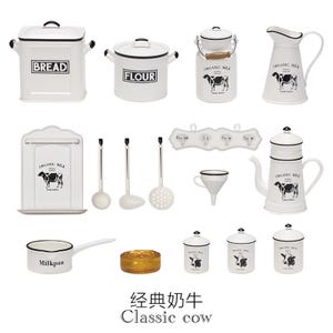 Puede incluir: Colección de utensilios de cocina blancos con detalles en negro, que incluyen recipientes para pan y harina, una jarra de leche y una cafetera. Los artículos presentan un gráfico de vaca y el texto "ORGANIC MILK".