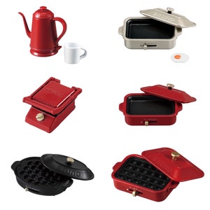 May include: A set of five red and black mini electric skillets with the word "BRUNO" printed on them. The skillets are designed for cooking small portions of food, such as pancakes, eggs, and other breakfast items.