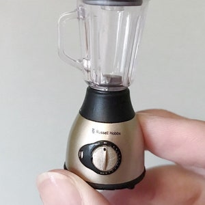 May include: A small, silver and black blender with a clear plastic container. The blender has a knob with settings for "Pulse", "Off", and "Max" and the brand name "Russell Hobbs" is printed on the side.