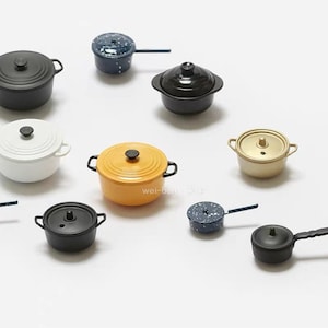 May include: A collection of miniature cookware, including pots and pans in various colors such as black, white, yellow, and speckled blue. Each piece has a lid and handles, showcasing a variety of designs and styles.