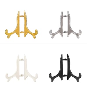 Puede incluir: Cuatro soportes de exhibición decorativos en dorado, plateado, blanco y negro. Cada soporte tiene un diseño simple y elegante con dos brazos curvos y una pieza central recta.