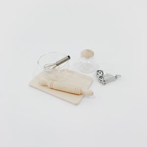 Puede incluir: Un conjunto de utensilios de cocina en miniatura para hornear, que incluye un rodillo, un tazón para mezclar con un batidor, un frasco de vidrio y cucharas medidoras.