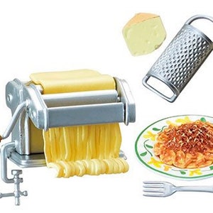 Op de afbeelding: Een zilveren pastamachine met een houten handvat, een blok kaas, een rasp, een bord spaghetti met tomatensaus en een vork. De pastamachine heeft een kruk en een klem om hem aan een tafel te bevestigen.