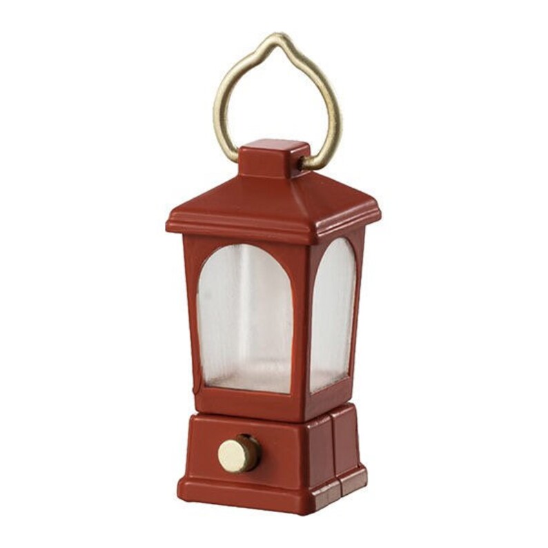 May include: A small, red lantern with a gold handle and a clear glass window. The lantern has a switch on the bottom.