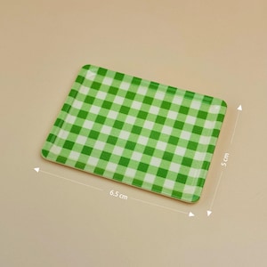 Puede incluir: Una bandeja rectangular con un patrón de cuadros verdes y blancos, de 6,5 cm por 5 cm. La bandeja tiene esquinas redondeadas y un acabado brillante. El diseño de cuadros es clásico, adecuado para servir o exhibir.
