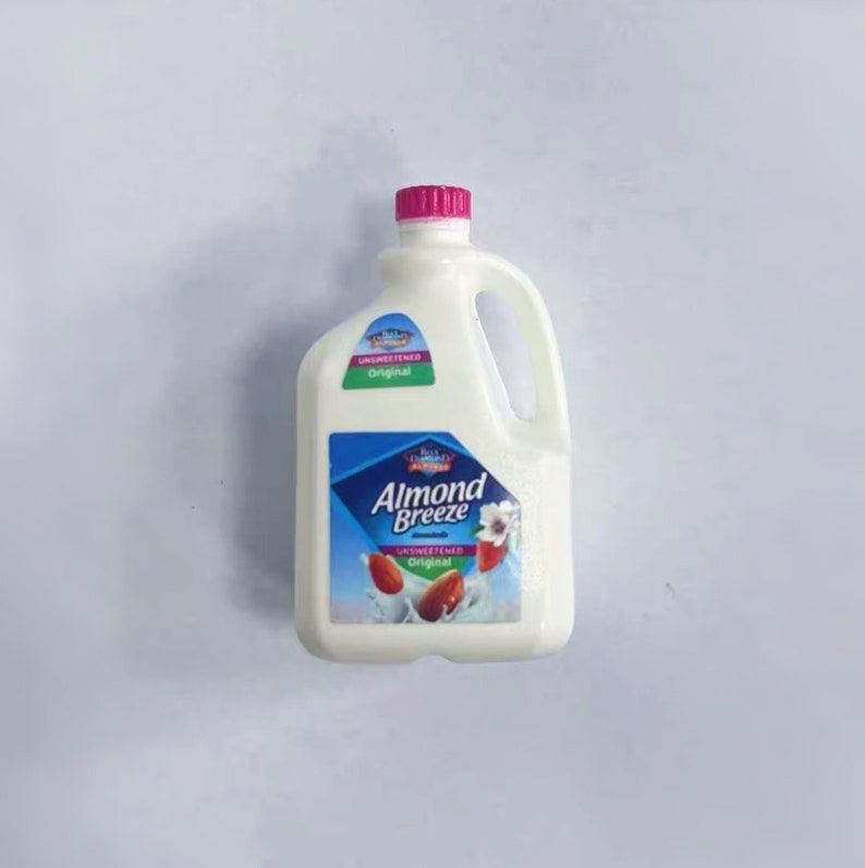 May include: A white plastic jug of Almond Breeze unsweetened almond milk. The jug has a pink cap and a handle. The label features a blue diamond with the brand name and images of almonds.