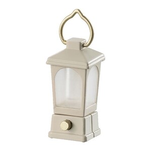 May include: A small, beige lantern with a gold handle and a clear glass window. The lantern has a small, round knob on the bottom.