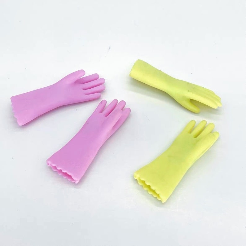 May include: Four rubber gloves in the image. Two are a light pink color, and two are a light yellow-green color. The gloves have a scalloped edge at the wrist and are lying on a white surface.