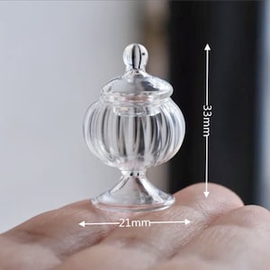 以下が含まれることがあります： 蓋と縦縞模様の透明なガラス瓶。瓶の高さは8.4cm、幅は5.3cmです。