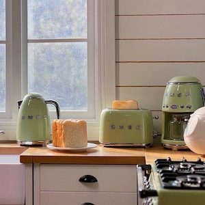 Peut inclure: Une cuisine avec des appareils SMEG vert pastel assortis. L'ensemble comprend une bouilloire, un grille-pain avec du pain grill&eacute;, une cafeti&egrave;re et un cuiseur &agrave; riz. Les appareils sont dispos&eacute;s sur un comptoir en bois devant une fen&ecirc;tre.