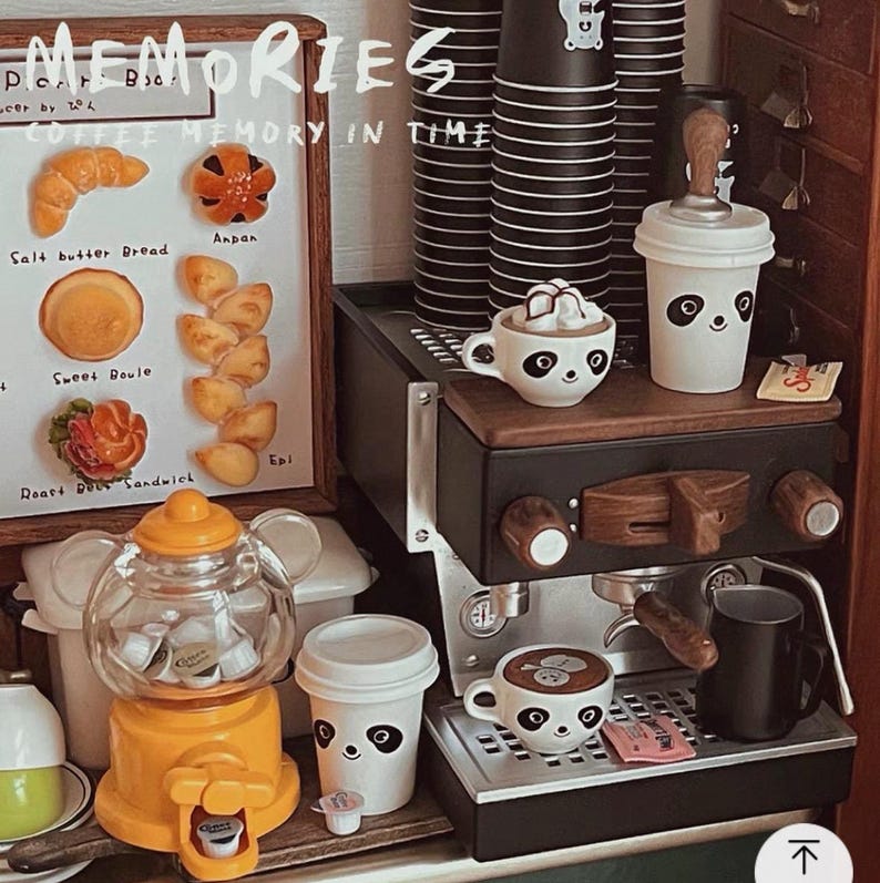 Pode incluir: Uma cena de caf&eacute; em miniatura com uma m&aacute;quina de caf&eacute; expresso preta, x&iacute;caras com rostos de panda e uma m&aacute;quina de chicletes. Uma placa exibe miniaturas de produtos de panifica&ccedil;&atilde;o. O texto "MEMORIES" e "COFFEE MEMORY IN TIME" s&atilde;o vis&iacute;veis.