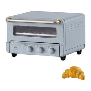 May include: A light blue toaster oven with a horizontal silver handle, a glass viewing window, and three control knobs on the front panel. The brand name Bruno is printed in gold on the left side. A single golden-brown croissant is placed below.