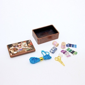 May include: A small wooden box with a printed image of sewing supplies, including spools of thread, buttons, and needles. The box is open and contains a variety of sewing supplies, including spools of thread, buttons, needles, and a pair of scissors.