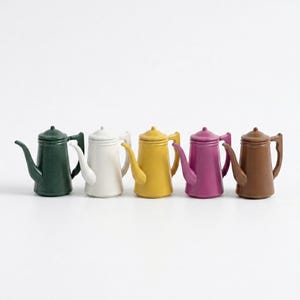 May include: Five small, colorful teapots in a row. The teapots are in shades of green, white, yellow, purple, and brown. Each teapot has a spout, handle, and lid. The teapots are on a white background.