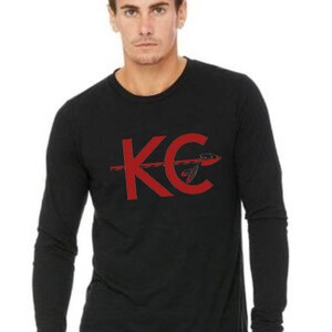 May include: Black long-sleeve shirt with a red graphic of the letters "KC" with an arrow through the "C".